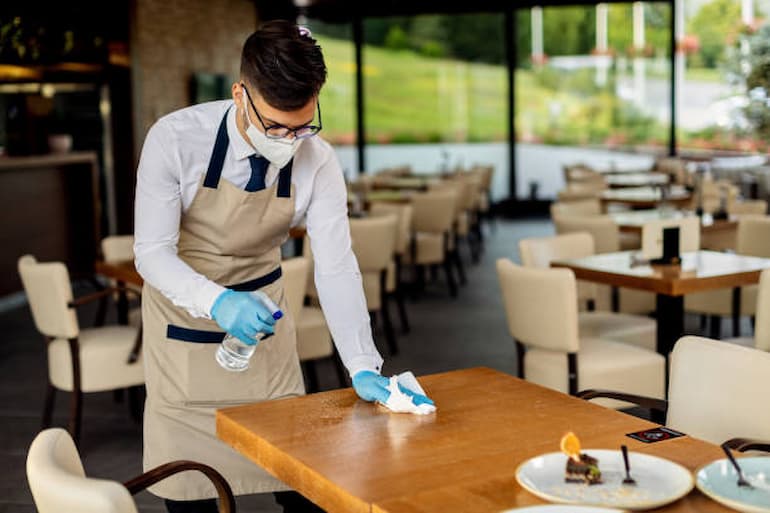 Waiter cleaning table in a restaurant wearing gloves and mask