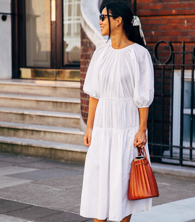 picture of a stylish woman wearing a white dress, a leather bag and a scrunchy on her hear