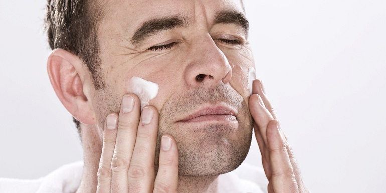Man wearing a bathrobe, relaxed, putting lotion on his face
